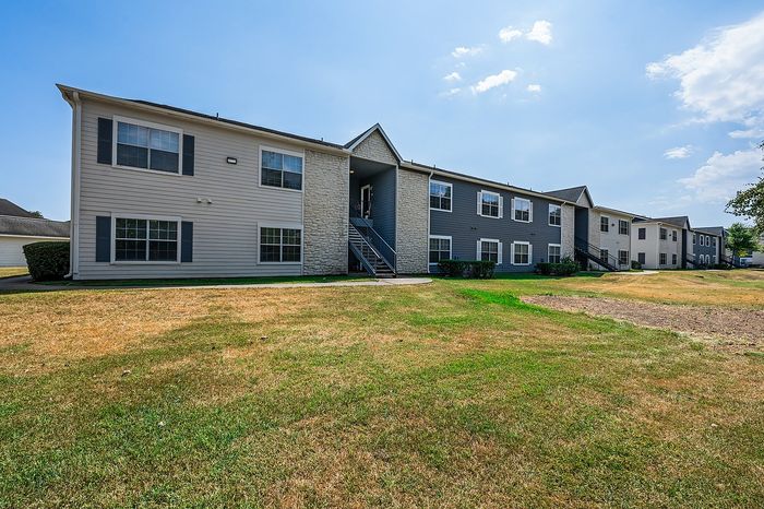 Charming two-story apartment building with attractive facade set in a serene grassy landscape under a bright blue sky.