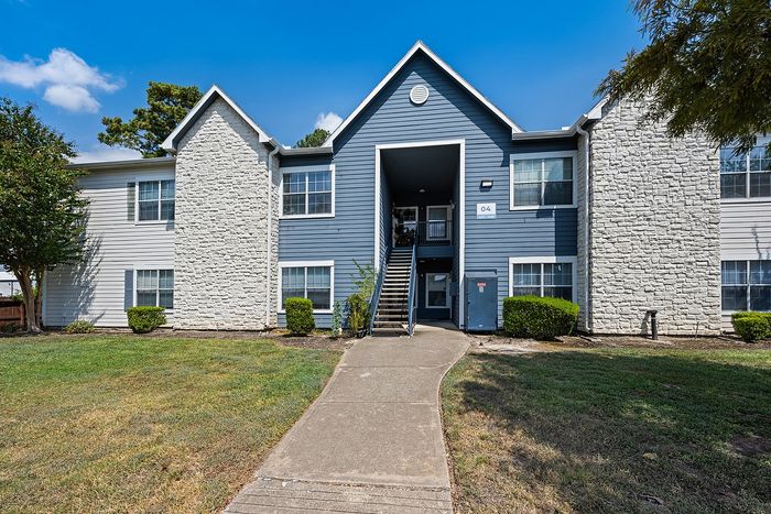 Charming apartment building with modern blue siding and white stone accents, surrounded by lush greenery and bright blue sky.