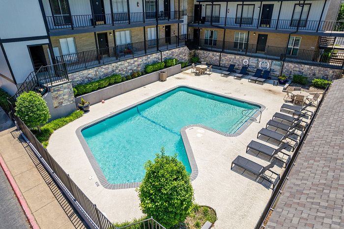 Charming apartment complex featuring a refreshing outdoor pool surrounded by stylish lounge chairs and cozy seating areas.