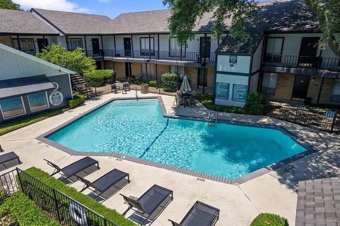 Inviting apartment complex with a sparkling outdoor pool, surrounded by comfortable lounge chairs and lush greenery, perfect for relaxation.