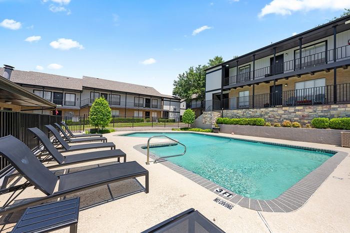 Charming apartment complex featuring a refreshing swimming pool, surrounded by lush greenery and modern lounge chairs for relaxing under the sun.