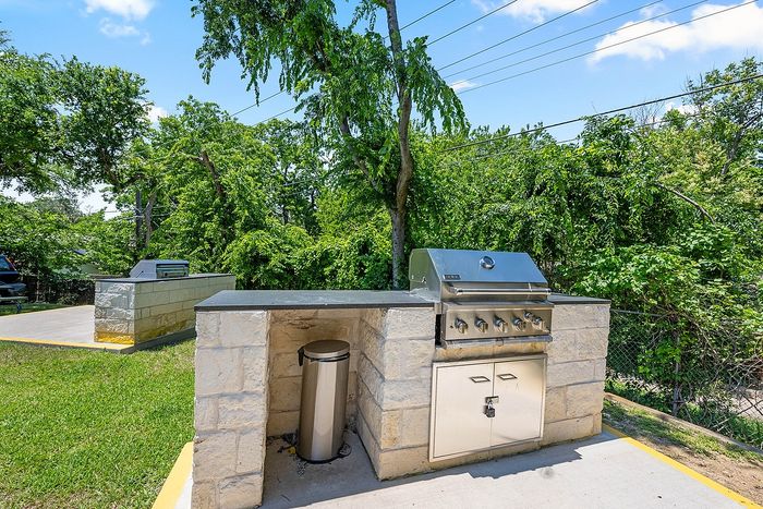 Modern outdoor grill station with stainless steel BBQ set amidst lush green trees, perfect for summer gatherings.