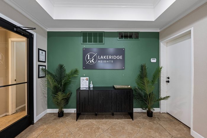 Elegant lobby entrance featuring a chic green accent wall with the Lakeridge Heights sign, flanked by lush plants and modern decor.