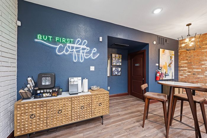 Chic coffee nook with a stylish neon 'But First Coffee' sign, complemented by a modern coffee machine and elegant wooden furnishings in a cozy apartment setting.