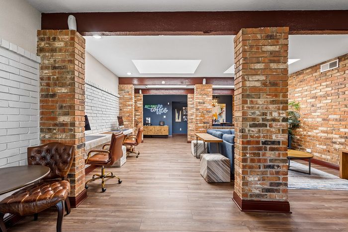 Elegant co-working space with leather chairs, brick accents, and modern lighting, offering a stylish work environment.