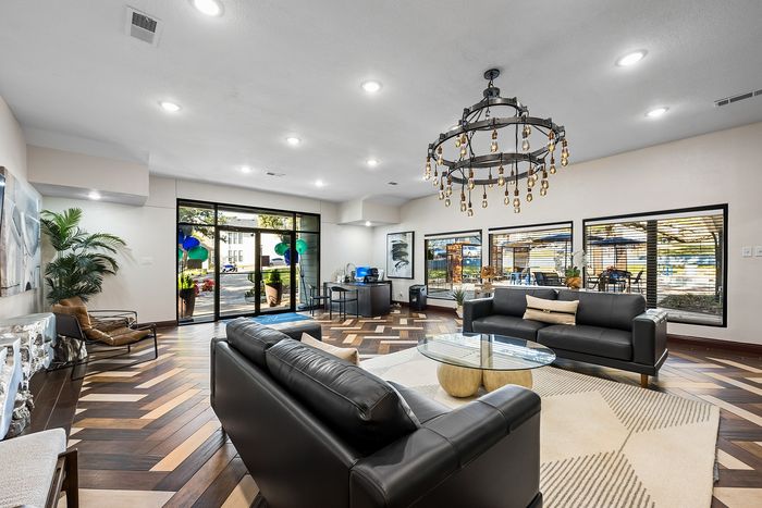 Luxurious living area with elegant leather sofas, a striking modern chandelier, and floor-to-ceiling windows offering a scenic outdoor view.