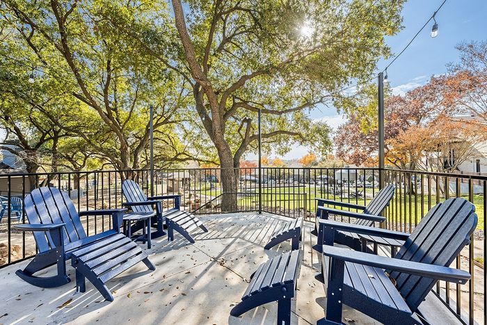 Charming outdoor patio with blue Adirondack chairs overlooking lush greenery and mature trees, perfect for relaxation.