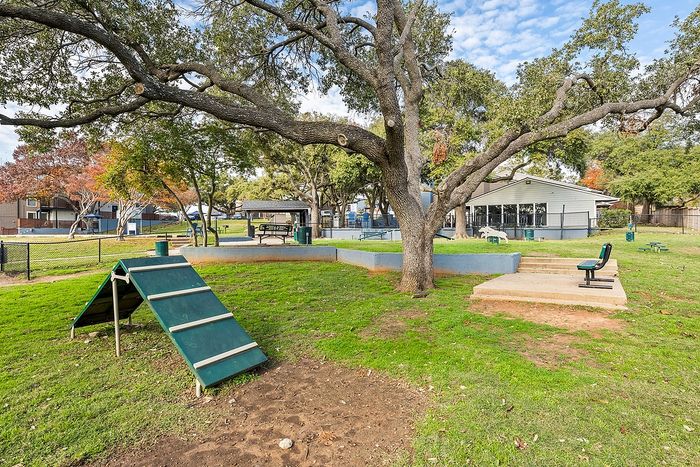 Expansive pet-friendly park area featuring agility equipment and lush landscaping, perfect for outdoor activities and relaxation.