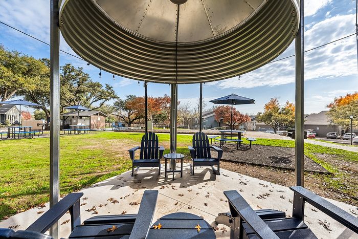 Inviting outdoor space with elegant lounge chairs under a modern gazebo, surrounded by lush greenery and vibrant autumn trees.