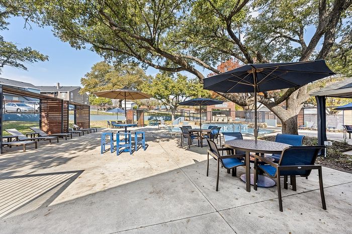 Inviting outdoor pool area with shaded seating and modern furniture, perfect for relaxation and social gatherings under lush trees.