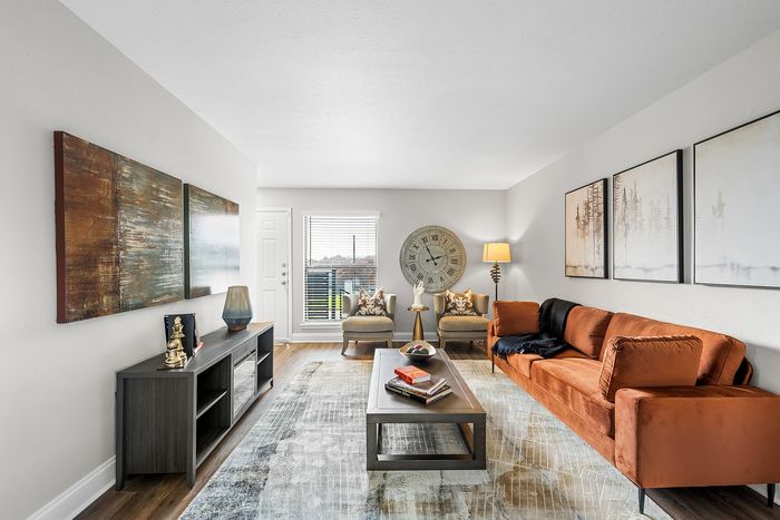 Bright and inviting living room with modern decor, featuring a plush orange sofa, elegant wall art, and a large window letting in natural light.