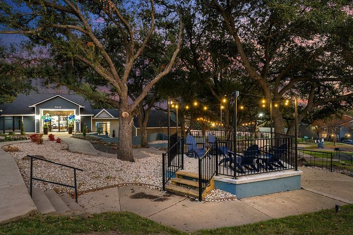 Charming outdoor communal space with twinkling string lights, surrounded by lush trees and modern architecture, perfect for relaxing evenings.