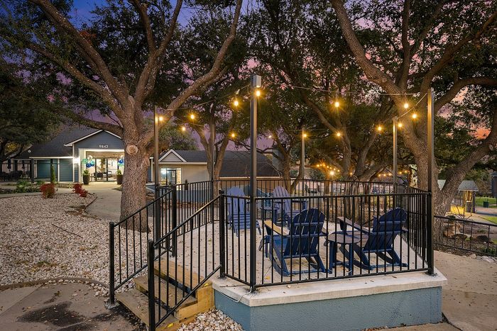 Charming outdoor patio with string lights and Adirondack chairs under a canopy of trees at twilight, creating a cozy ambiance.