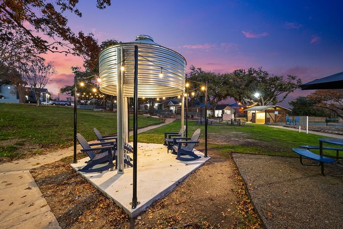 Charming outdoor seating area with string lights under a stylish gazebo, set in a lush green park at dusk, perfect for relaxation and gatherings.