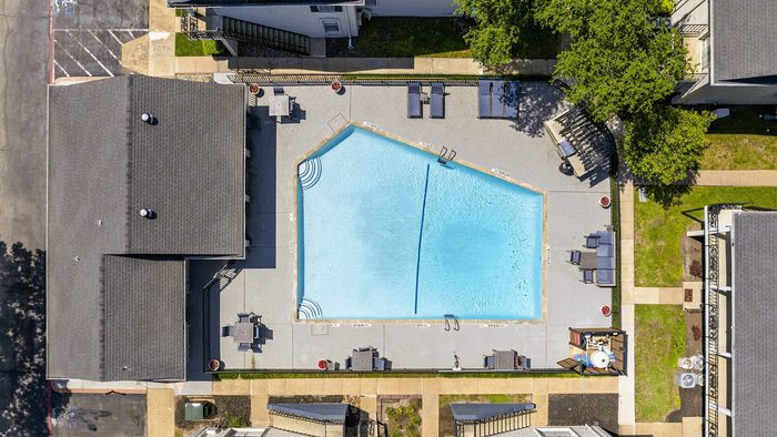 Charming aerial view of a beautifully maintained apartment complex pool area surrounded by greenery and cozy lounge seating.