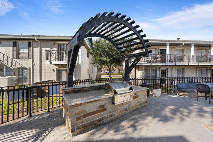 Charming apartment courtyard featuring a modern outdoor grill area with stylish seating and a unique arched pergola.
