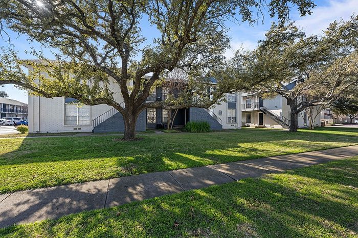 Charming apartment complex with mature oak trees and spacious green lawns, offering a serene residential setting.