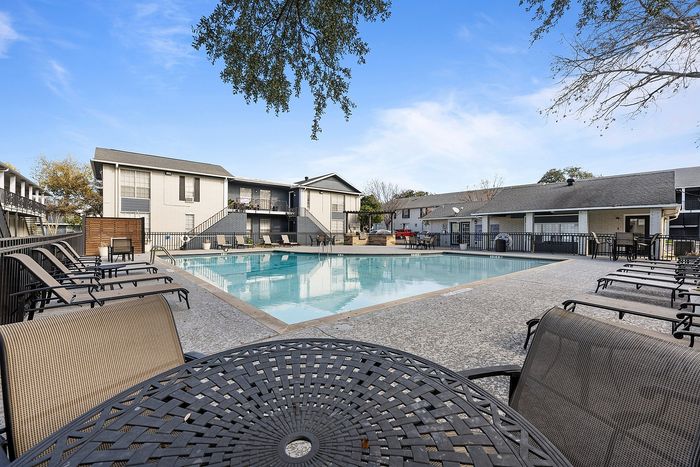 Inviting apartment complex showcasing a serene swimming pool surrounded by comfortable lounge chairs, perfect for relaxation under a clear blue sky.