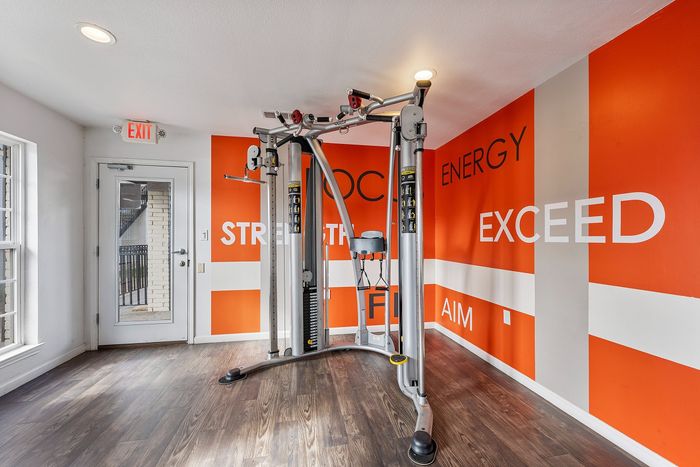 Bright and modern fitness room with professional gym equipment and motivational decor on vibrant orange walls.