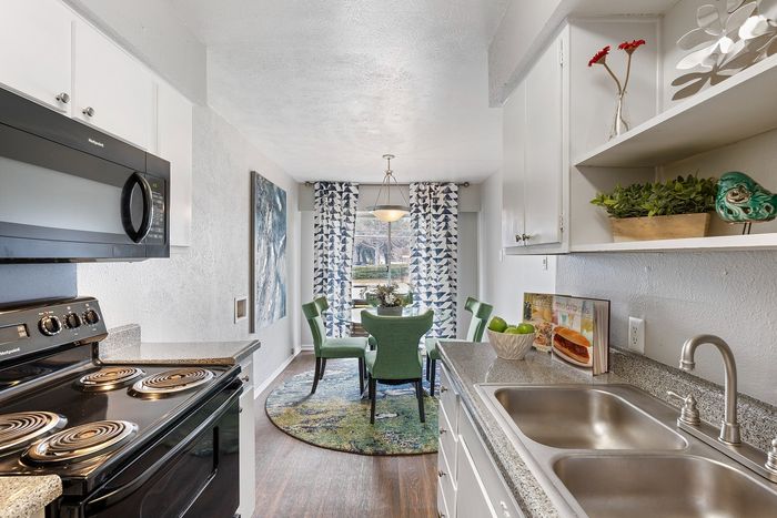 Bright and modern kitchen with sleek appliances, granite countertops, and an inviting dining area featuring elegant green chairs and a stylish glass table.