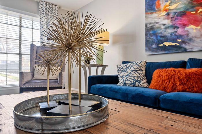 Stylish modern living room showcasing a plush blue sofa with vibrant cushions, abstract wall art, and an elegant metal sculpture on a wooden coffee table.