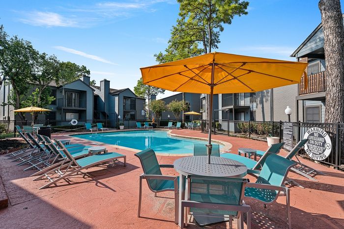 Inviting apartment pool area with modern lounging chairs, vibrant yellow umbrellas, and serene outdoor seating, perfect for relaxation and summer gatherings.