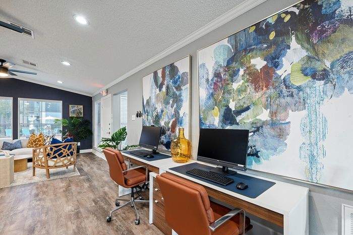 Contemporary living room with stylish seating, vibrant abstract art, and sleek workstation setup.