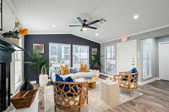 Inviting living room with modern decor, featuring stylish chairs, plush sofa with vibrant pillows, and a sleek ceiling fan, all illuminated by natural light through large windows.