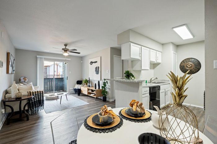 Bright and modern open living space featuring a cozy seating area, elegant dining setup, and a sleek kitchen with white cabinetry.