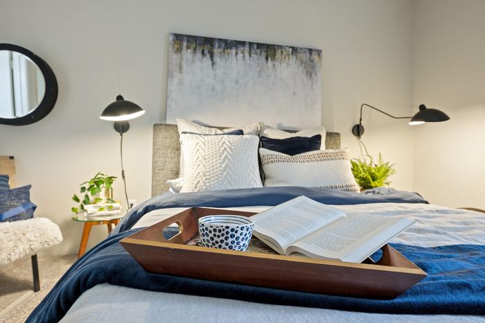 Elegant bedroom with cozy bedding, stylish wall art, and ambient lighting, featuring a wooden tray with a book and cup.