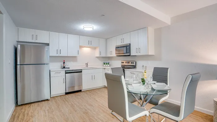 Modern kitchen and dining area with sleek stainless steel appliances, elegant white cabinetry, and a cozy dining setup on stylish wooden flooring.