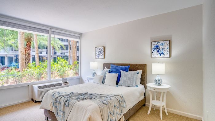 Bright and inviting bedroom with elegant decor, showcasing large windows with views of lush palms and outdoor seating.
