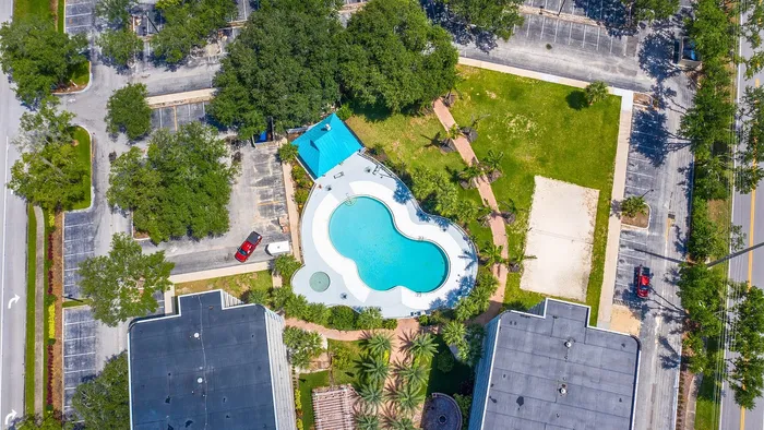 Aerial view of a luxury apartment complex with a uniquely shaped pool, vibrant green spaces, and ample parking.