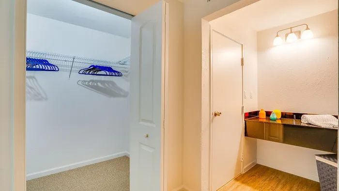 Inviting apartment entryway featuring a spacious walk-in closet with blue hangers and a well-lit vanity area, perfect for organization and elegance.