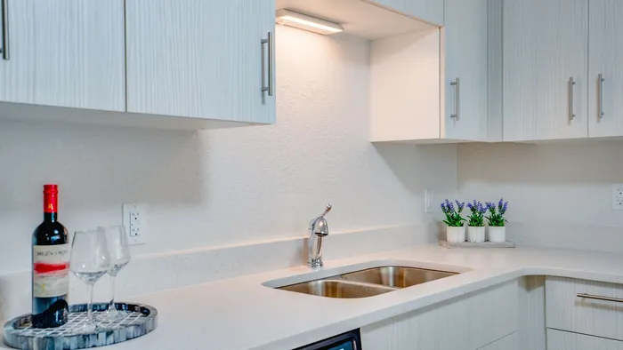 Modern kitchen with sleek white cabinets, stainless steel sink, and elegant under-cabinet lighting. Accented with wine and glass setup, perfect for intimate gatherings.