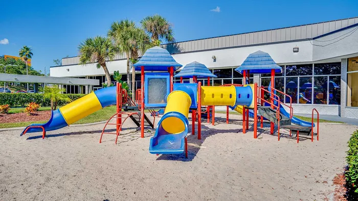 Vibrant outdoor playground with colorful slides and climbing structures set in a sunny and lush landscaped area.