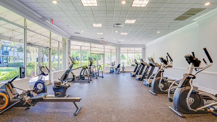 Bright and spacious gym with modern exercise equipment and floor-to-ceiling windows offering lush garden views.