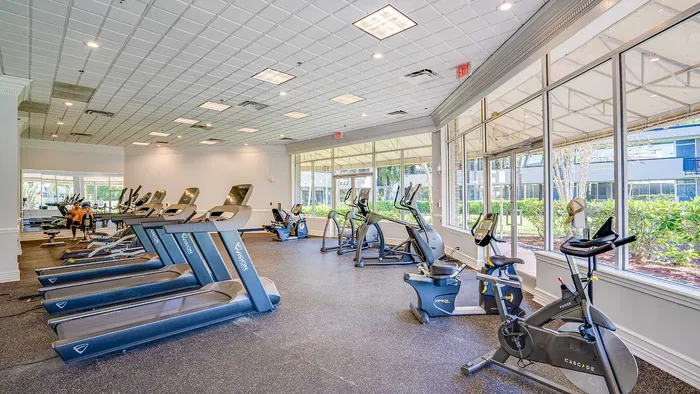 Modern fitness center with state-of-the-art treadmills, stationary bikes, and elliptical machines in a bright, spacious room with large windows.