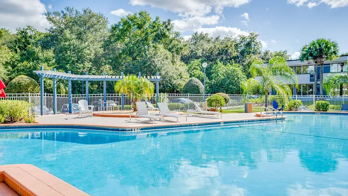Inviting outdoor swimming pool with lounging area surrounded by lush greenery and clear blue skies for a perfect relaxation spot.
