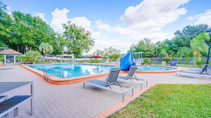 Inviting outdoor pool area with sleek lounge chairs, surrounded by lush greenery and bright blue skies.