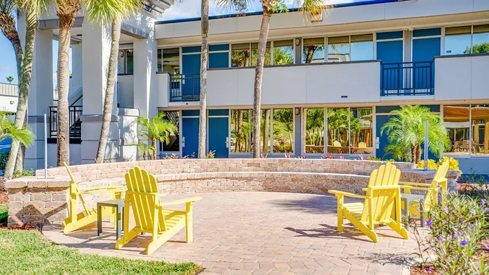 Charming outdoor patio with vibrant yellow chairs and lush palm trees in a modern apartment complex.
