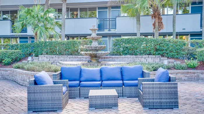 Inviting outdoor seating area with modern wicker furniture and a decorative fountain, surrounded by lush greenery.