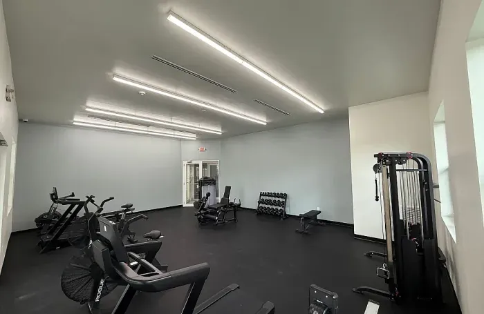 Wide view of a bright apartment fitness center with exercise machines and open floor space.
