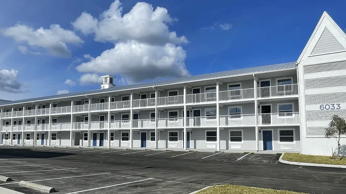 Modern three-story apartment complex with striking blue doors, ample parking, and a bright, inviting exterior under a clear blue sky.