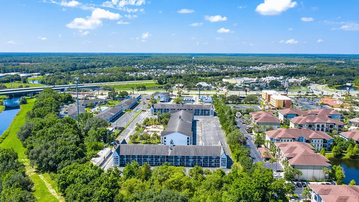 Aerial view of a vibrant apartment complex surrounded by lush greenery and scenic landscapes, with convenient proximity to major roads.