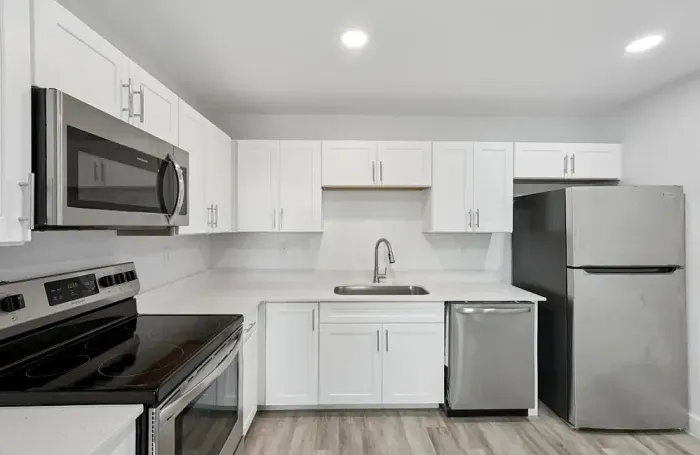Modern apartment kitchen featuring stainless steel appliances, dark countertops, and white cabinetry.