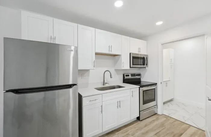 Modern apartment kitchen featuring stainless steel appliances, dark countertops, and white cabinetry.