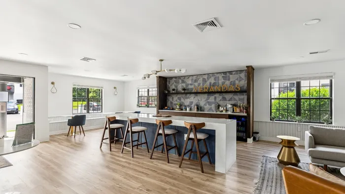 Bright and inviting communal area featuring modern bar seating, elegant lighting, and large windows with lush garden views.