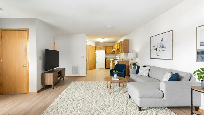 Bright and inviting living space with a cozy gray sectional, modern decor, and an open-plan kitchen, enhancing comfort and style.