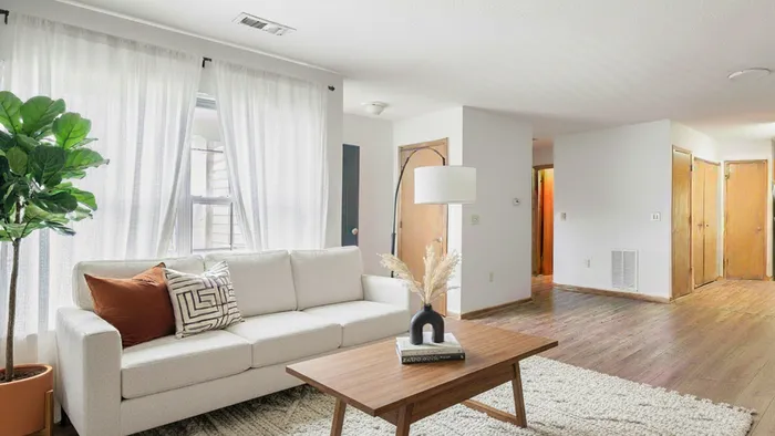 Inviting living room with a chic white sofa, vibrant throw pillows, elegant floor lamp, and lush green plant by the window, creating a cozy and stylish ambiance.